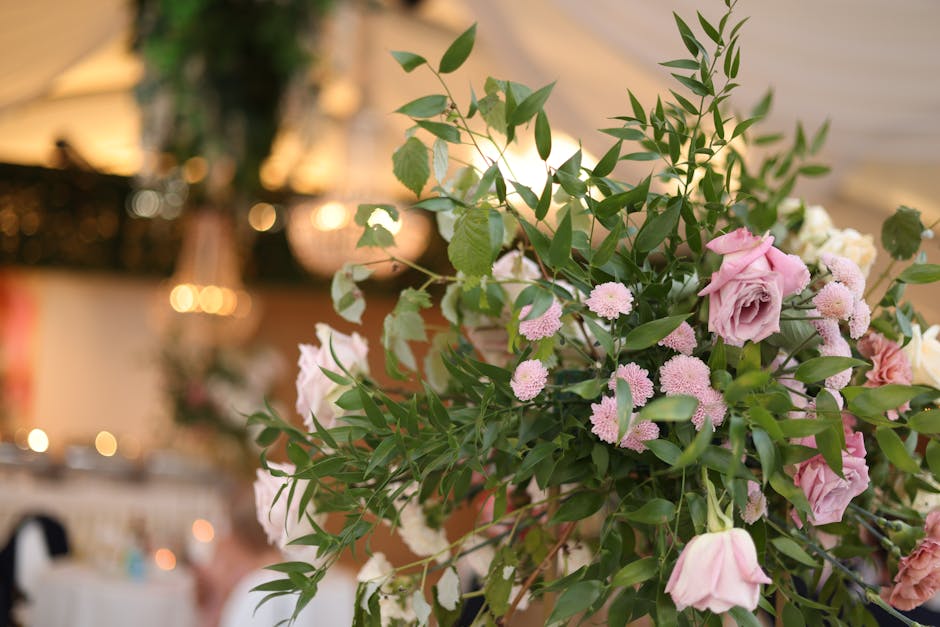 A close-up view of a floral arrangement featuring soft pink roses, small pale pink chrysanthemums, and lush green foliage arranged in a natural, cascading style. The flowers are fresh, with delicate p